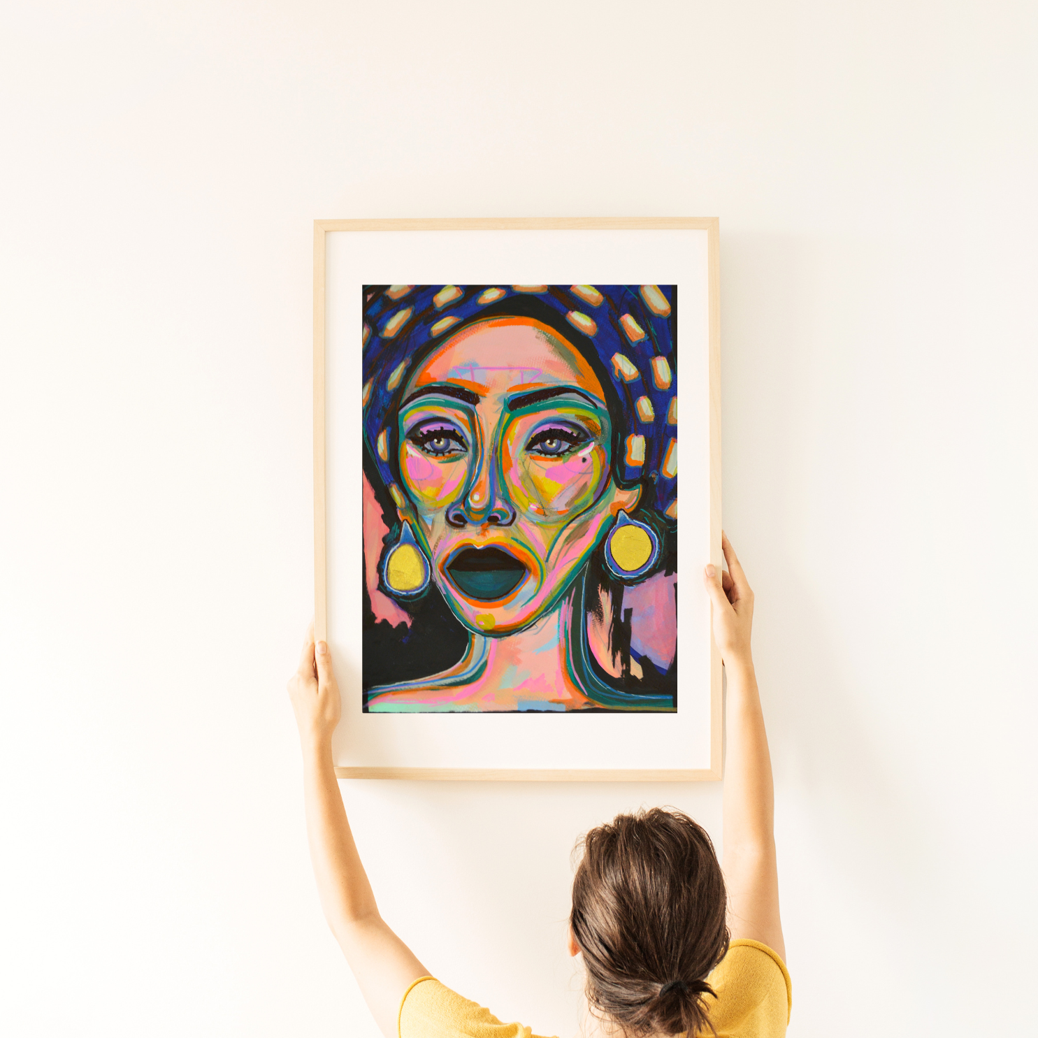 daria painting of beautiful lady on paper pink blue gold and spots. framed in light wood being hung on a white wall 